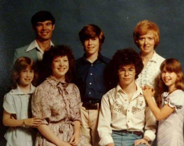 A 1980s family portrait of two parents and their five children smiling in a studio before AI photo enhancement